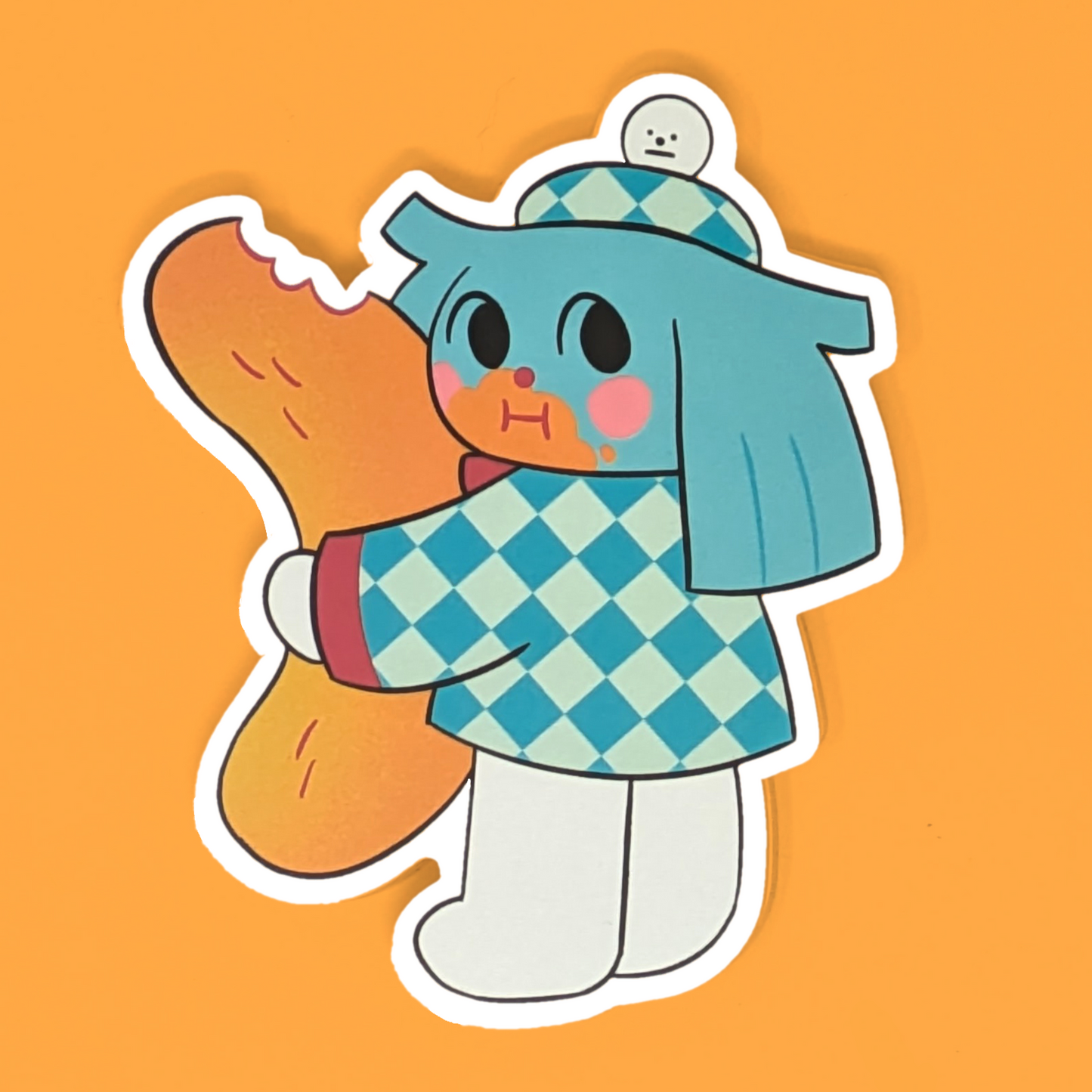 A vinyl sticker of a cartoon character resembling a cheetah with a human-like body, wearing a blue and white checkered outfit, holding a snack