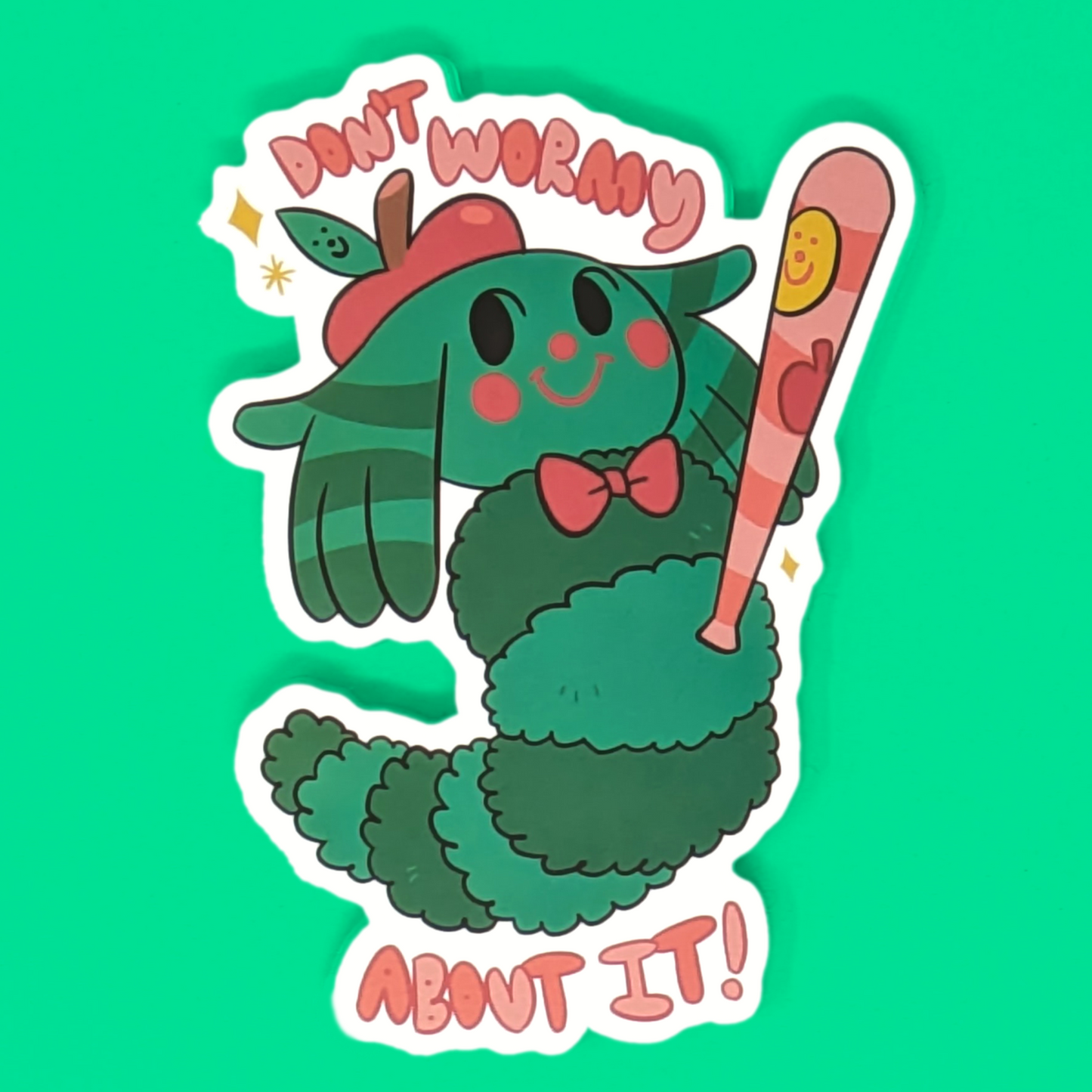 A vinyl sticker featuring a cartoon-style green caterpillar with a red hat and bow tie, holding a baseball bat, on a teal background with the text 'DON'T WORMY ABOUT IT'.